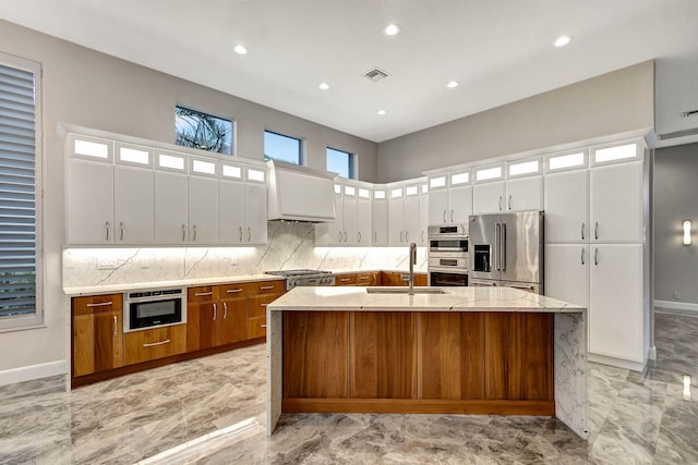 kitchen featuring white cabinets, light stone counters, stainless steel appliances, and a kitchen island with sink