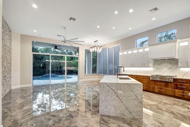 kitchen featuring stainless steel gas stovetop, white cabinetry, sink, and a kitchen island with sink