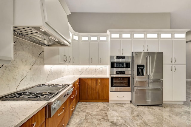 kitchen featuring appliances with stainless steel finishes, backsplash, light stone counters, custom range hood, and white cabinets