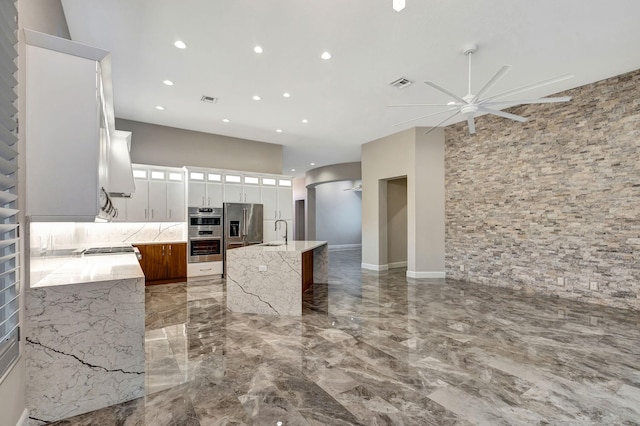 kitchen featuring light stone countertops, appliances with stainless steel finishes, sink, white cabinets, and an island with sink