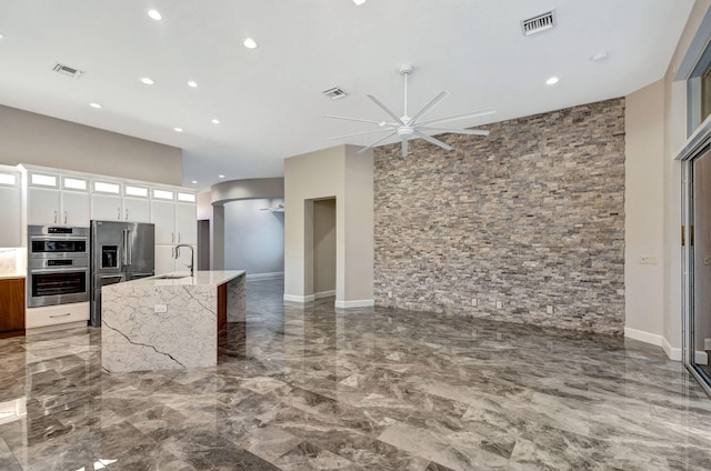 kitchen with appliances with stainless steel finishes, light stone counters, ceiling fan, sink, and white cabinets