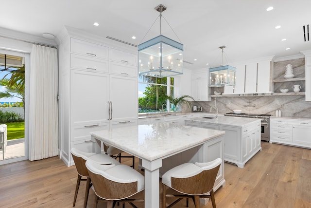 kitchen featuring sink, light wood-type flooring, a kitchen island, decorative light fixtures, and high end stove