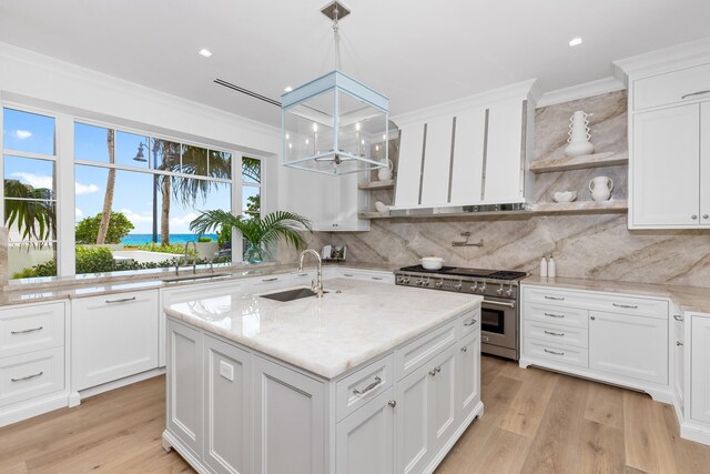 kitchen featuring high end range, ornamental molding, sink, a center island with sink, and white cabinetry