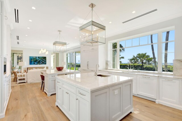 kitchen featuring a sink, an island with sink, a chandelier, white cabinetry, and crown molding