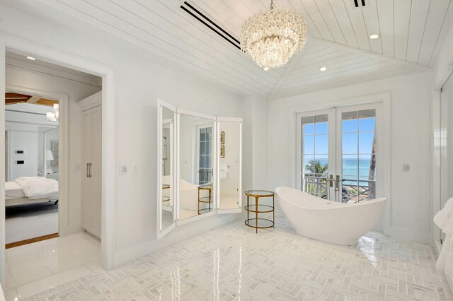 full bath featuring a chandelier, a water view, a freestanding bath, french doors, and lofted ceiling