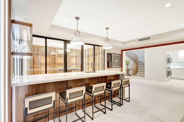 kitchen with a raised ceiling, stacked washing machine and dryer, a sink, light stone countertops, and recessed lighting