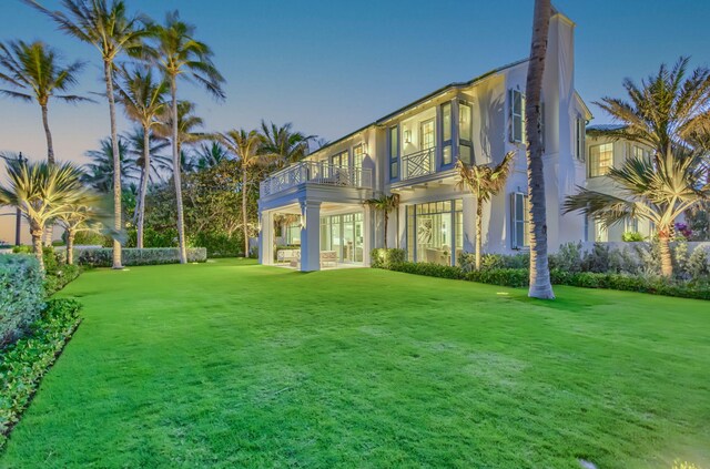 rear view of property with a balcony, french doors, a lawn, and stucco siding
