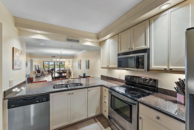 kitchen featuring appliances with stainless steel finishes, sink, kitchen peninsula, dark stone counters, and a notable chandelier