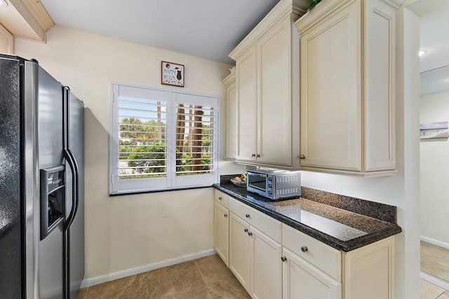 kitchen with dark stone countertops, light tile patterned flooring, cream cabinets, and stainless steel fridge with ice dispenser