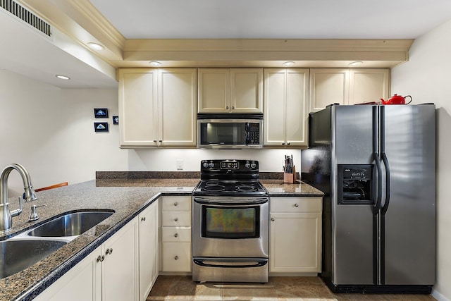 kitchen with cream cabinets, stainless steel appliances, sink, and dark stone counters