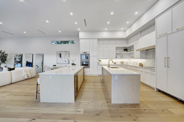 kitchen with a spacious island, light hardwood / wood-style floors, stainless steel double oven, and white cabinets