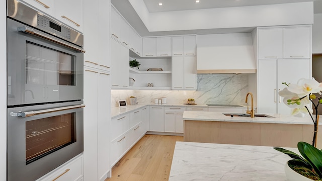 kitchen featuring stainless steel double oven, light hardwood / wood-style flooring, sink, white cabinets, and light stone counters