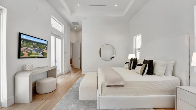 bedroom with a high ceiling, a tray ceiling, and light wood-type flooring