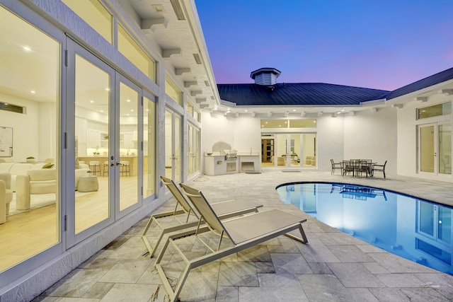 pool at dusk featuring french doors, a patio, and area for grilling