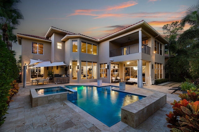 back house at dusk with a patio area, a balcony, ceiling fan, outdoor lounge area, and a swimming pool with hot tub