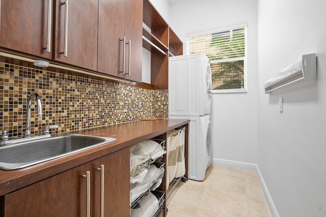 laundry area with sink, light tile patterned flooring, stacked washer / drying machine, and cabinets