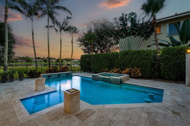 pool at dusk with an in ground hot tub and a patio area