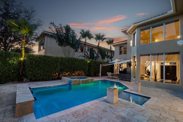 pool at dusk featuring an in ground hot tub and a patio