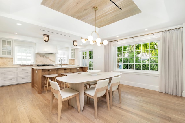 dining space featuring sink, light hardwood / wood-style flooring, a raised ceiling, and a wealth of natural light