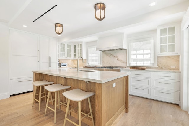 kitchen featuring sink, a spacious island, plenty of natural light, white cabinetry, and custom exhaust hood