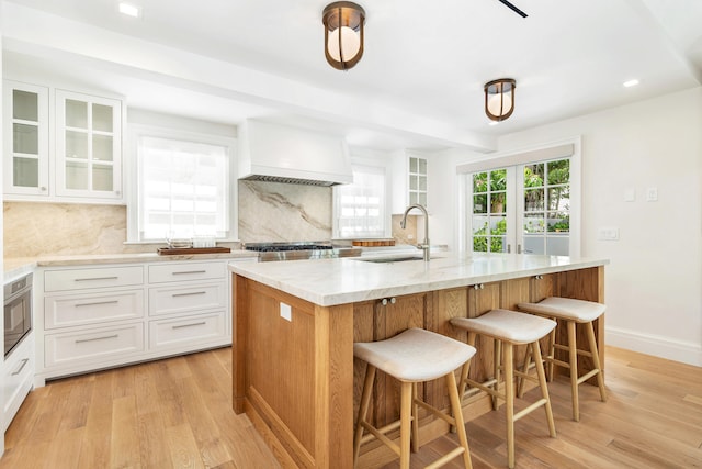 kitchen featuring a center island with sink, sink, white cabinets, and light wood-type flooring