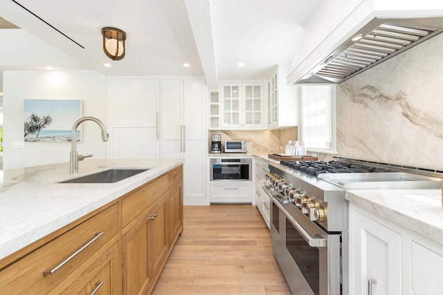 kitchen with white cabinetry, custom range hood, stainless steel appliances, and sink