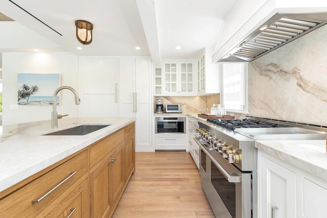 284 Monterey Rd, Palm Beach, FL 33480 - kitchen with appliances with stainless steel finishes, a sink, wall chimney range hood, light wood finished floors, and decorative backsplash