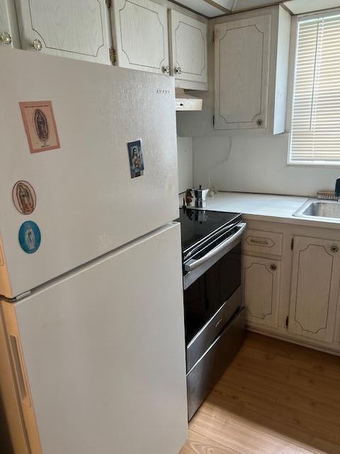 kitchen with range hood, sink, stainless steel range with electric cooktop, white fridge, and light hardwood / wood-style floors