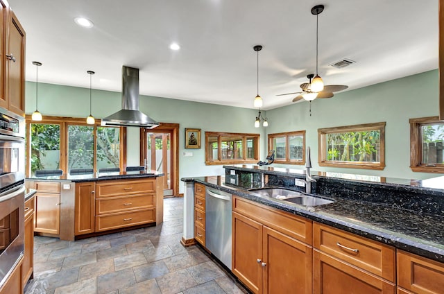 kitchen with dark stone counters, island range hood, stainless steel appliances, decorative light fixtures, and sink