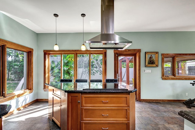 kitchen with dark stone countertops, island exhaust hood, a healthy amount of sunlight, and pendant lighting