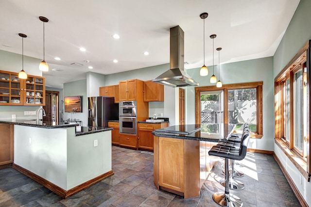 kitchen featuring island exhaust hood, a kitchen bar, stainless steel appliances, and dark stone counters