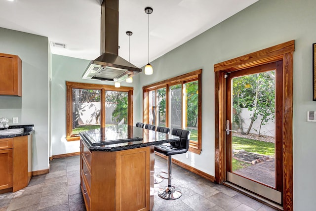 kitchen featuring a kitchen island, island exhaust hood, a breakfast bar area, dark stone countertops, and decorative light fixtures