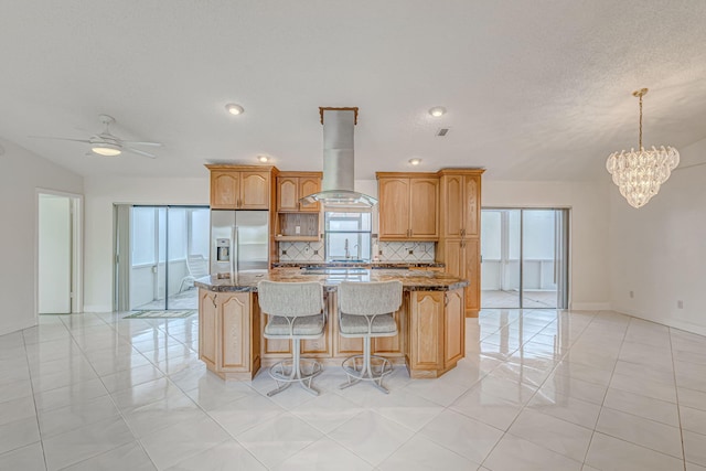 kitchen with stainless steel fridge, a center island, island range hood, and dark stone counters