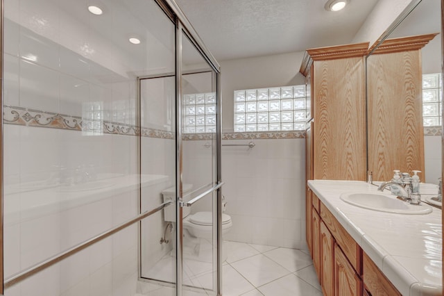 bathroom with a shower with door, tile patterned floors, toilet, tile walls, and vanity