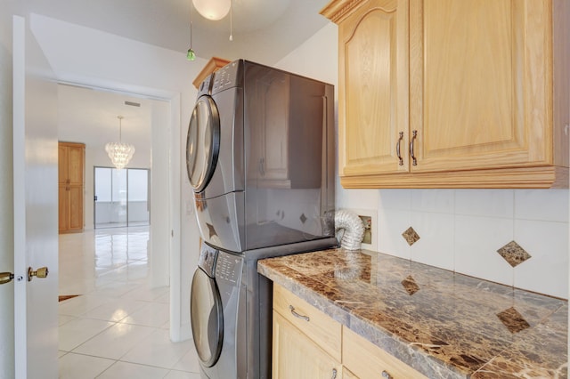 laundry room featuring light tile patterned floors, cabinets, stacked washer and clothes dryer, and an inviting chandelier