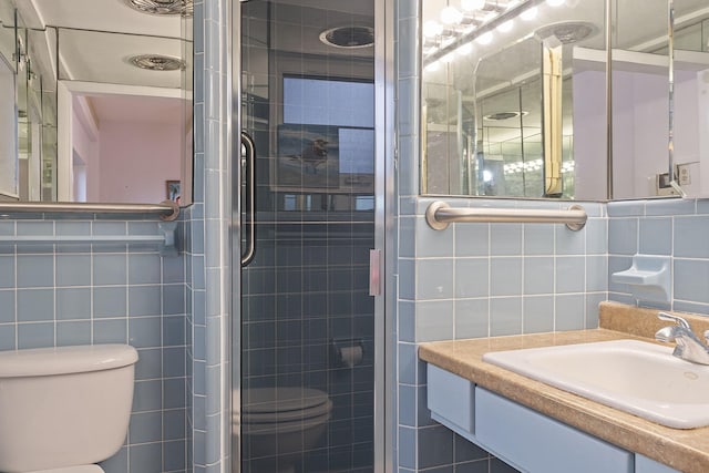 bathroom with vanity, toilet, tile walls, and a shower with shower door