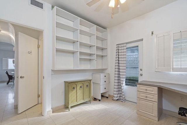 unfurnished office featuring ceiling fan, light tile patterned flooring, and built in desk