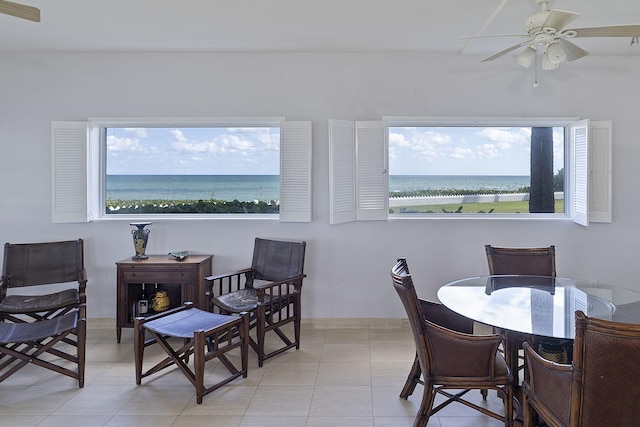 dining space with ceiling fan, a beach view, a water view, and light tile patterned floors