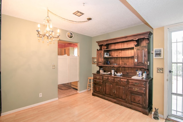 interior space featuring a textured ceiling, dark brown cabinets, a notable chandelier, and light wood-type flooring