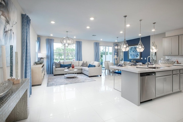 kitchen with a kitchen island with sink, gray cabinetry, sink, decorative light fixtures, and stainless steel dishwasher