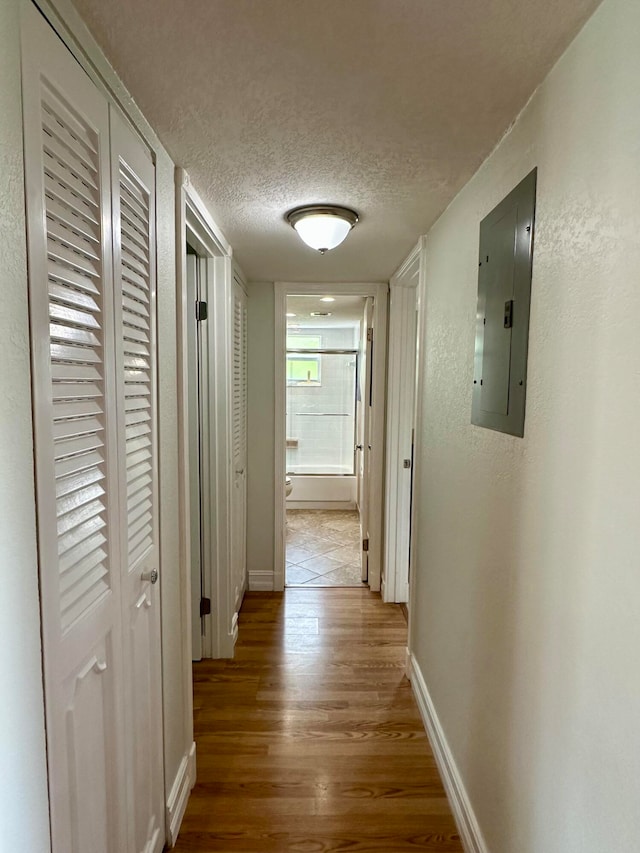 hall with electric panel, wood-type flooring, and a textured ceiling