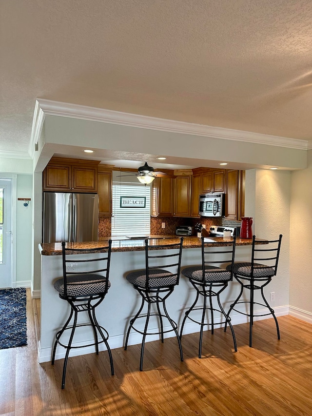 kitchen with crown molding, tasteful backsplash, stainless steel appliances, and a kitchen bar