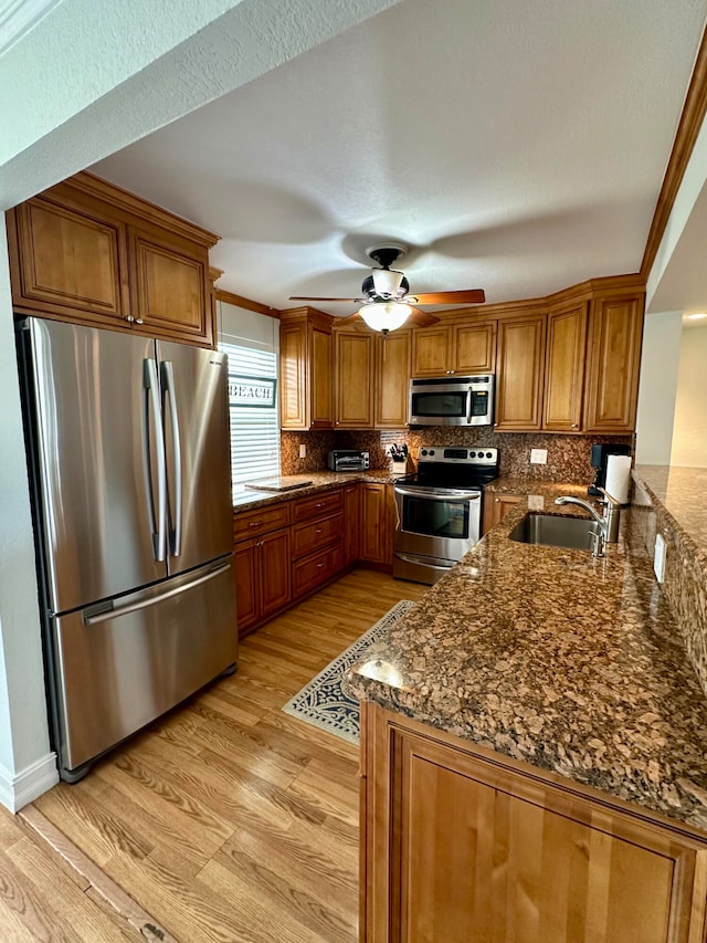 kitchen with appliances with stainless steel finishes, dark stone counters, light hardwood / wood-style flooring, ornamental molding, and sink