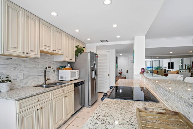 kitchen with light stone countertops, stainless steel appliances, sink, and cream cabinetry