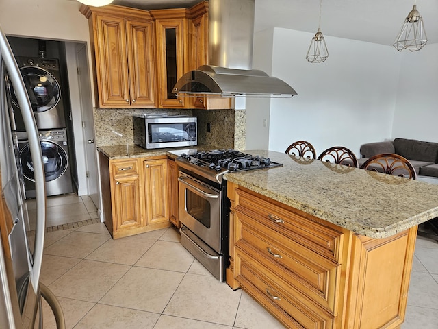 kitchen featuring backsplash, island range hood, stainless steel appliances, light tile patterned floors, and stacked washer and dryer