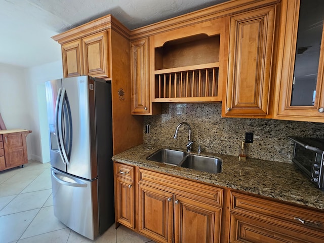 kitchen featuring tasteful backsplash, dark stone counters, sink, light tile patterned floors, and stainless steel fridge with ice dispenser