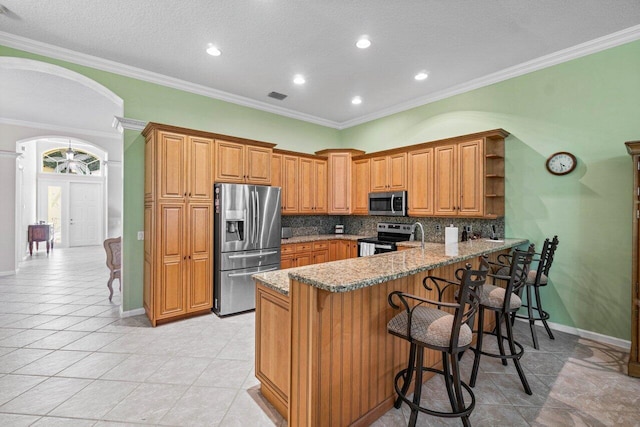 kitchen with light stone counters, kitchen peninsula, stainless steel appliances, a breakfast bar, and backsplash