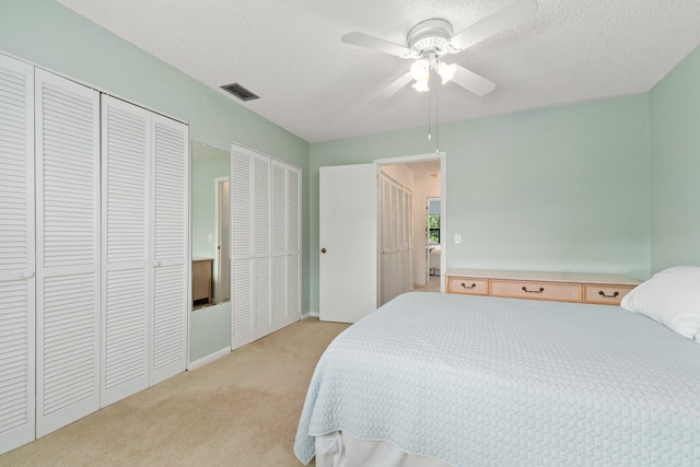 bedroom featuring a textured ceiling, two closets, light colored carpet, and ceiling fan