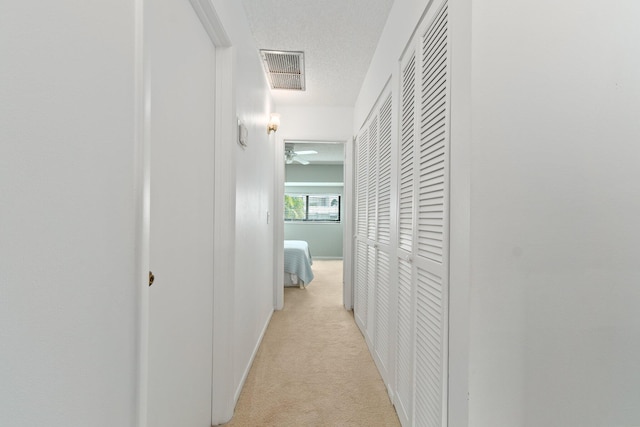 hallway featuring light colored carpet, a textured ceiling, visible vents, and baseboards