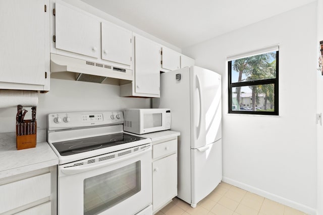 kitchen featuring light countertops, baseboards, under cabinet range hood, and white appliances